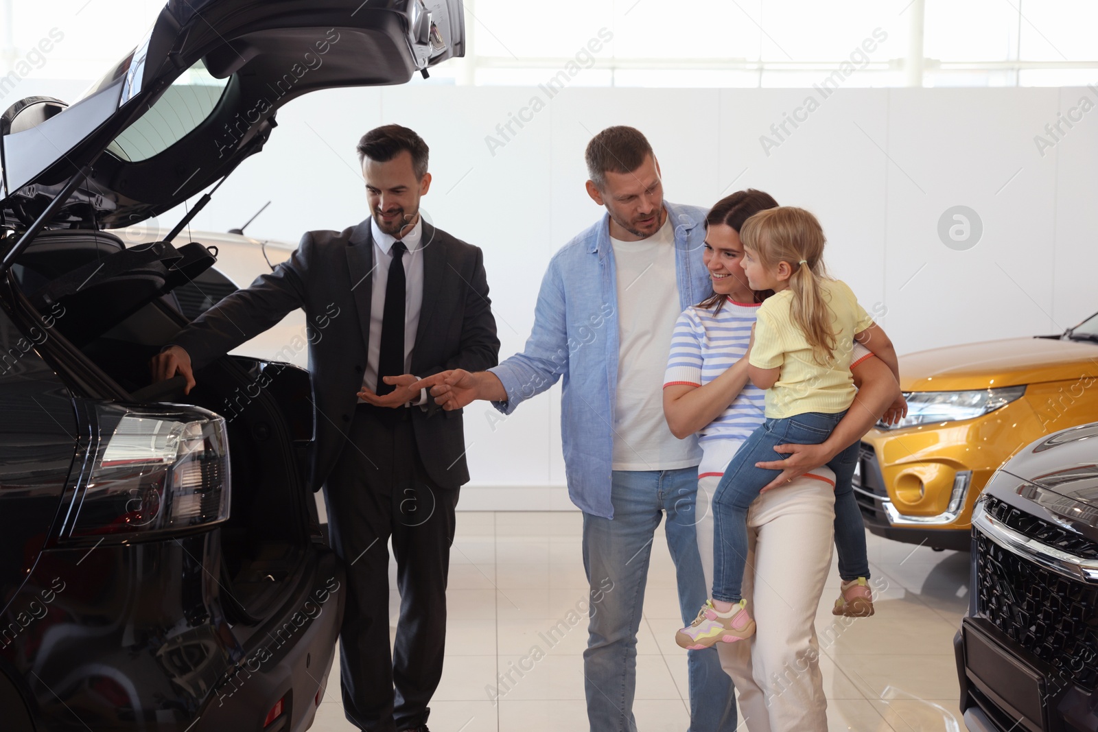 Photo of Salesman showing new car to happy family in salon
