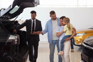 Photo of Salesman showing new car to happy family in salon