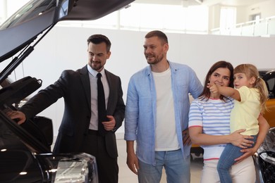 Photo of Salesman showing new car to happy family in salon