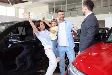 Photo of Salesman giving car key to happy family in salon