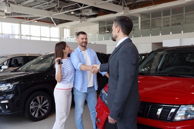 Photo of Salesman shaking hands with happy family near new car in salon