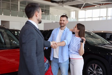 Photo of Salesman shaking hands with happy family near new car in salon