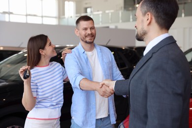 Photo of Salesman shaking hands with happy family near new car in salon