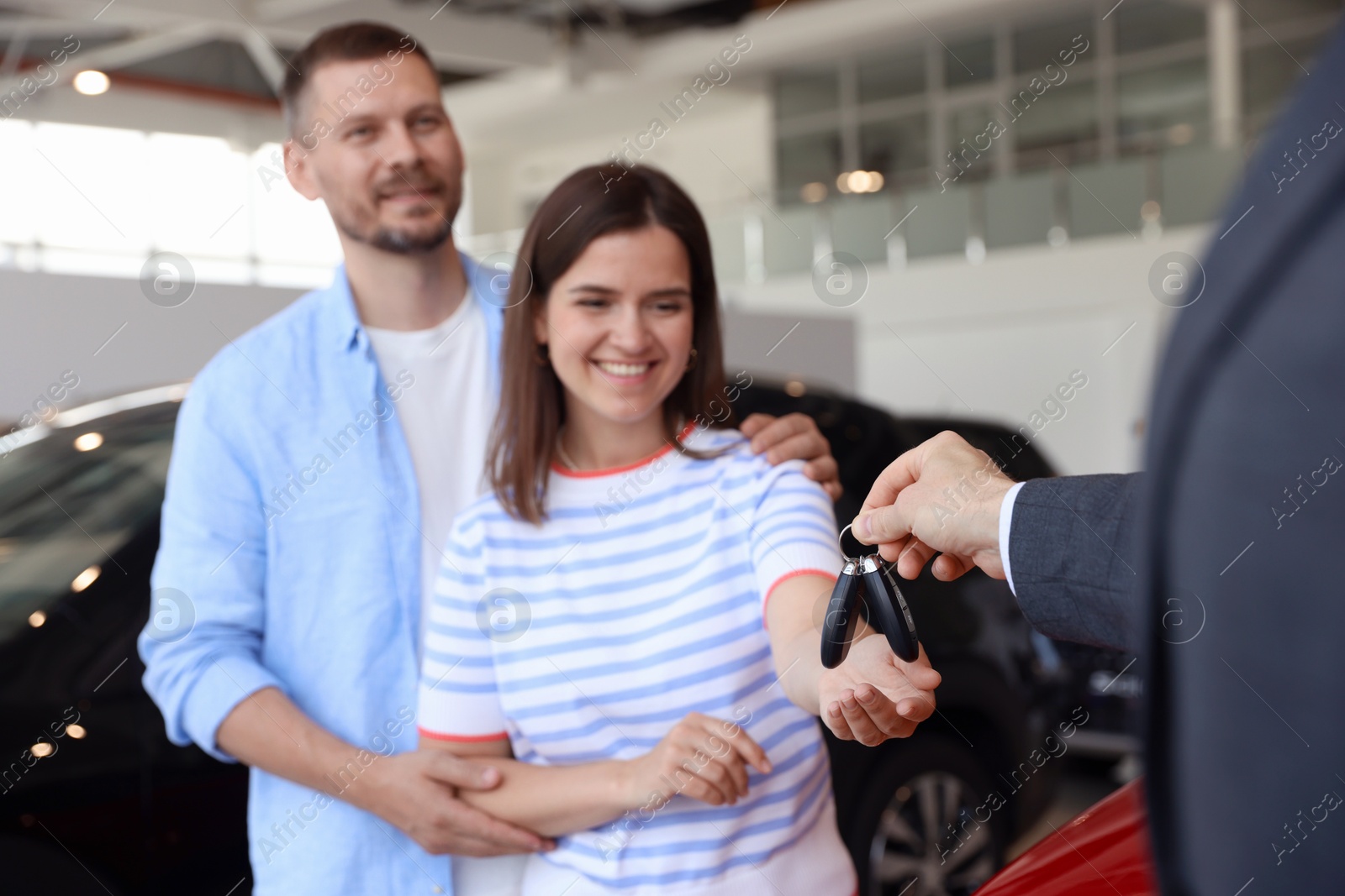Photo of Salesman giving car key to happy family in salon, selective focus