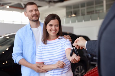 Photo of Salesman giving car key to happy family in salon, selective focus