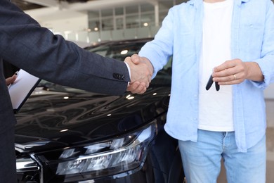 Photo of Salesman shaking hands with man near new car in salon, closeup