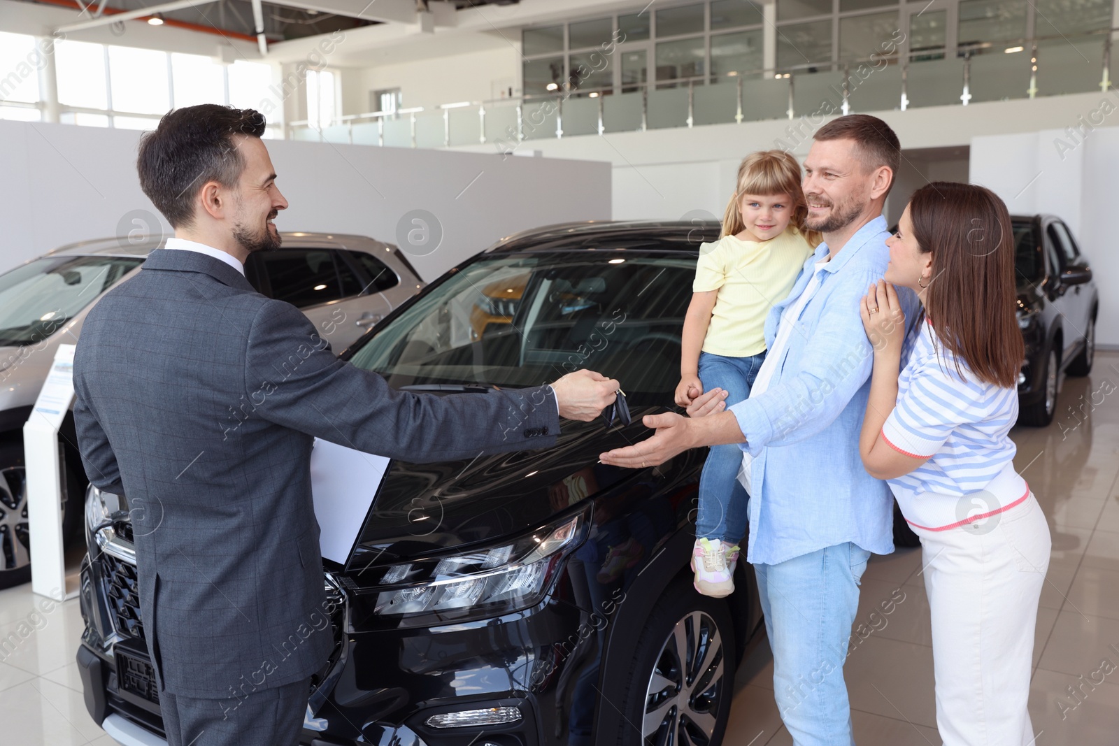 Photo of Salesman giving car key to happy family in salon