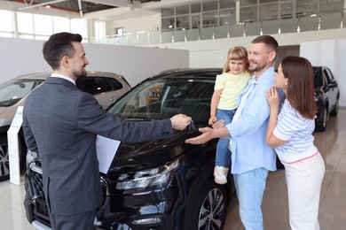 Photo of Salesman giving car key to happy family in salon