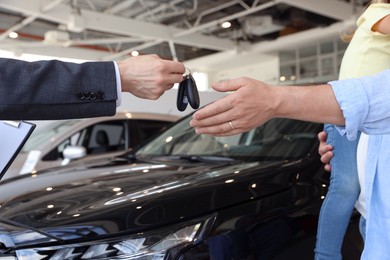 Photo of Salesman giving car key to family in salon, closeup