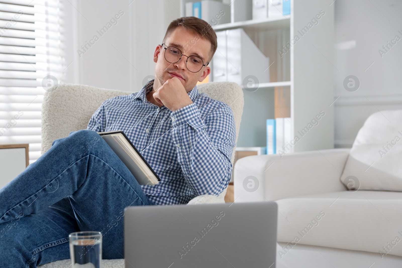 Photo of Psychologist in glasses with notepad during online session by laptop in office