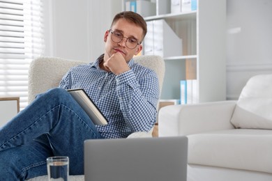 Photo of Psychologist in glasses with notepad during online session by laptop in office