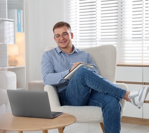 Photo of Smiling psychologist in glasses with notepad during online session by laptop in office