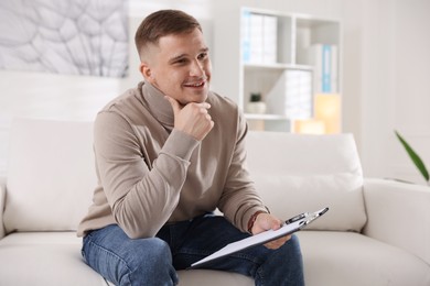 Photo of Smiling psychologist with clipboard on sofa in office
