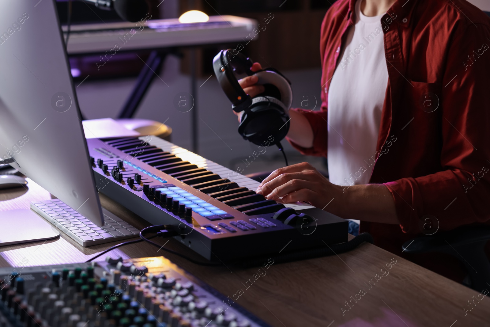 Photo of Man with headphones working with MIDI keyboard at table indoors, closeup