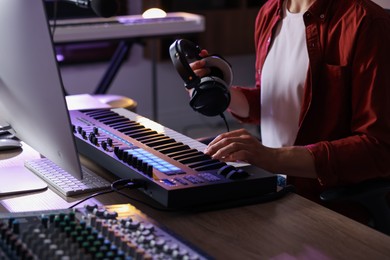 Photo of Man with headphones working with MIDI keyboard at table indoors, closeup