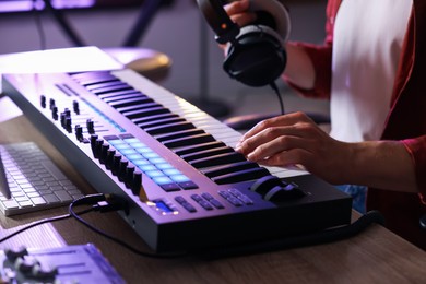 Photo of Man with headphones working with MIDI keyboard at table indoors, closeup