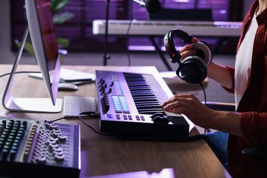 Photo of Man with headphones working with MIDI keyboard at table indoors, closeup