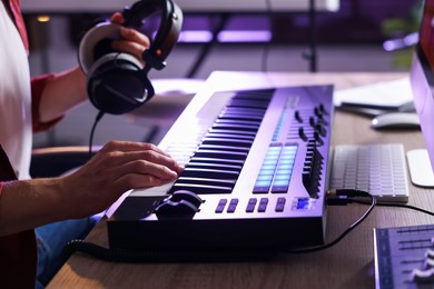 Photo of Man with headphones working with MIDI keyboard at table indoors, closeup
