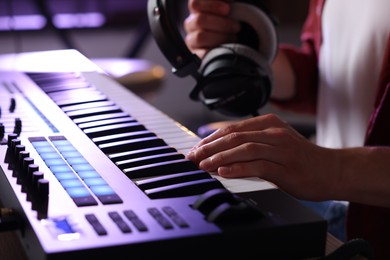 Photo of Man with headphones working with MIDI keyboard at table indoors, closeup