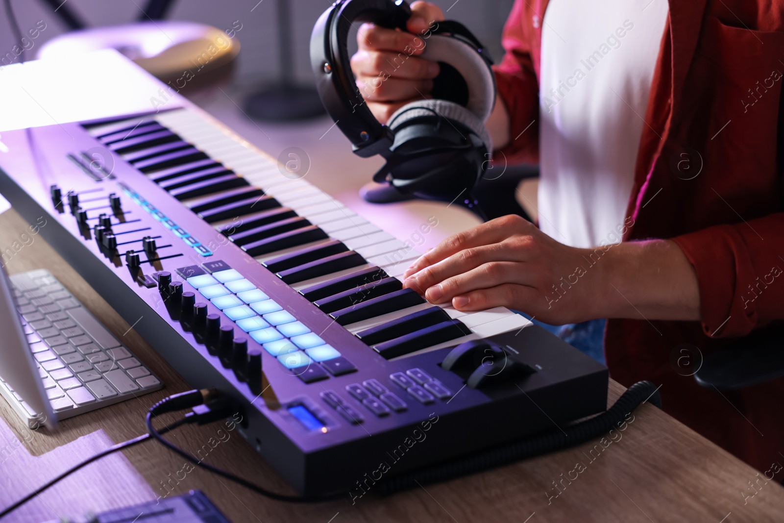 Photo of Man with headphones working with MIDI keyboard at table indoors, closeup