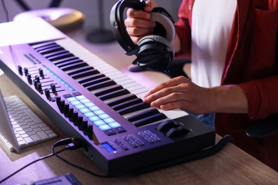 Photo of Man with headphones working with MIDI keyboard at table indoors, closeup