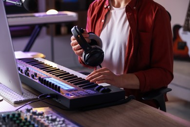 Photo of Man with headphones working with MIDI keyboard at table indoors, closeup