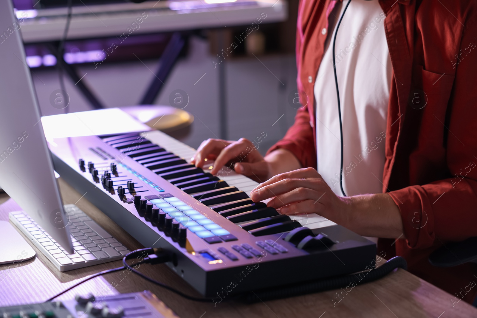 Photo of Man working with MIDI keyboard at wooden table indoors, closeup