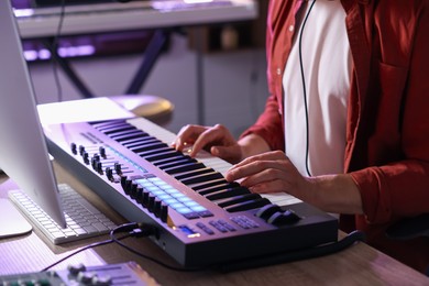 Photo of Man working with MIDI keyboard at wooden table indoors, closeup