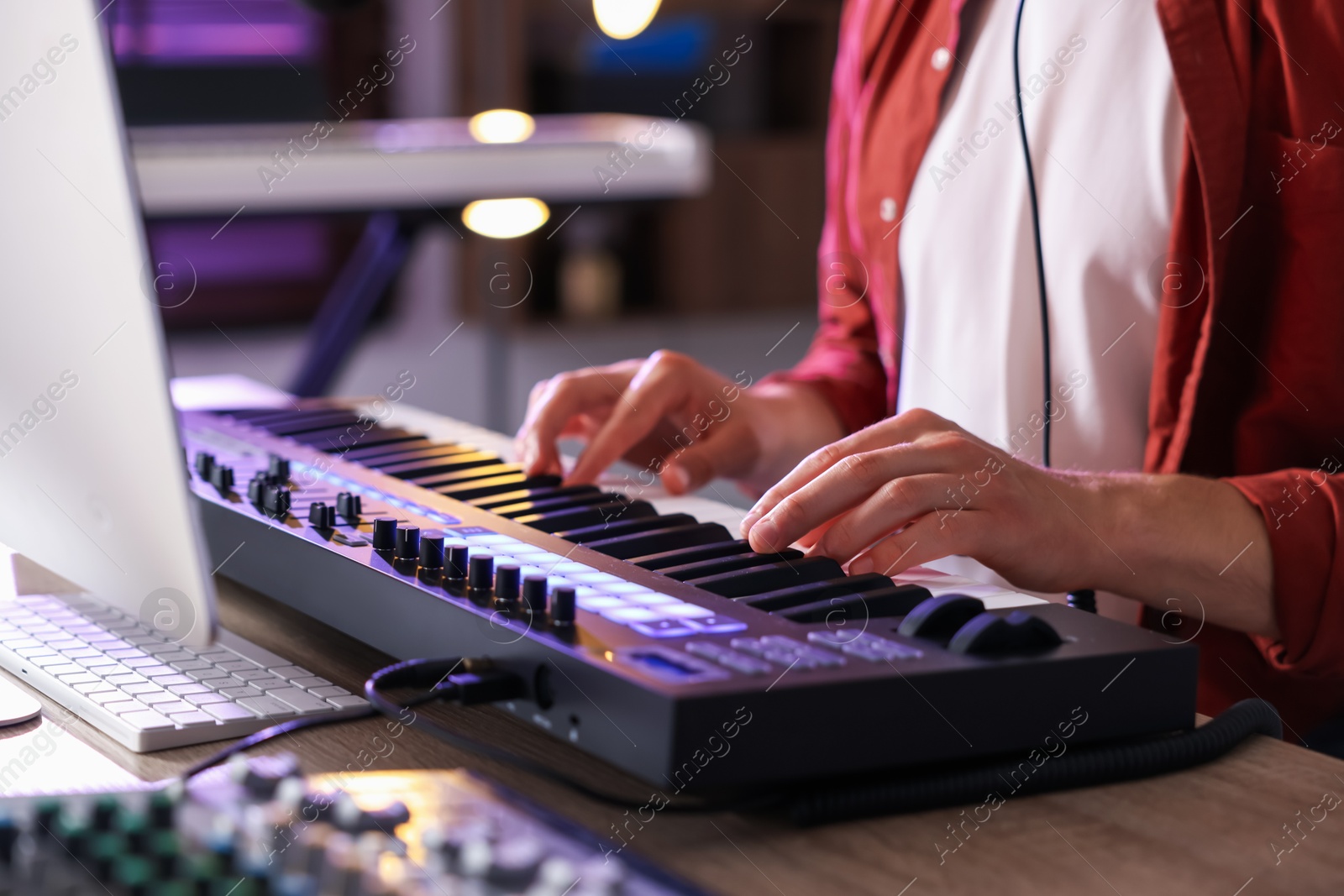 Photo of Man working with MIDI keyboard at wooden table indoors, closeup