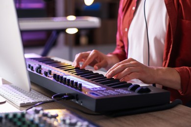 Photo of Man working with MIDI keyboard at wooden table indoors, closeup