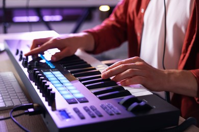 Photo of Man working with MIDI keyboard at table indoors, closeup