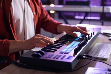 Photo of Man working with MIDI keyboard at wooden table indoors, closeup