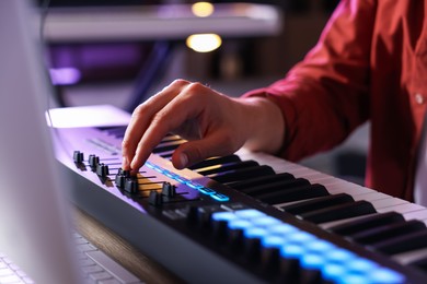 Photo of Man working with MIDI keyboard at table indoors, closeup