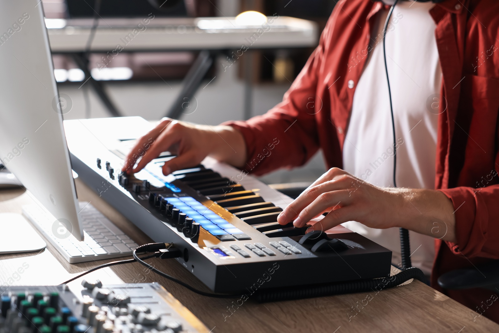 Photo of Man working with MIDI keyboard at wooden table indoors, closeup