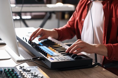 Photo of Man working with MIDI keyboard at wooden table indoors, closeup