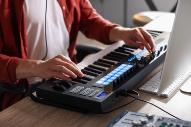 Photo of Man working with MIDI keyboard at wooden table indoors, closeup