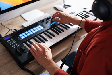 Photo of Man working with MIDI keyboard at wooden table indoors, above view