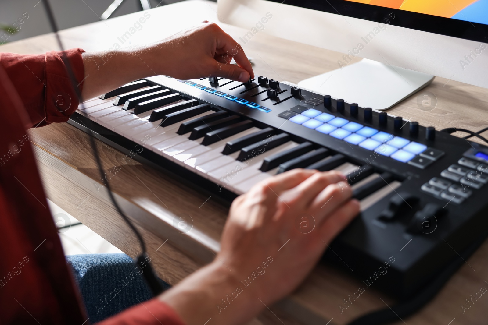 Photo of Man working with MIDI keyboard at wooden table indoors, closeup