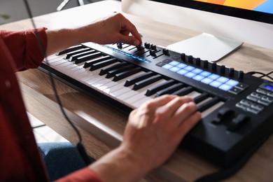 Photo of Man working with MIDI keyboard at wooden table indoors, closeup