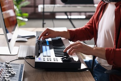 Photo of Man working with MIDI keyboard at wooden table indoors, closeup