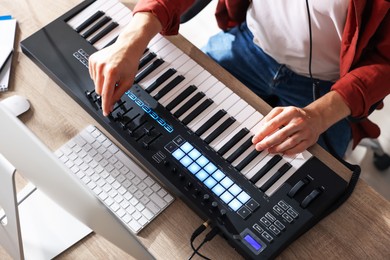 Photo of Man working with MIDI keyboard at wooden table indoors, above view