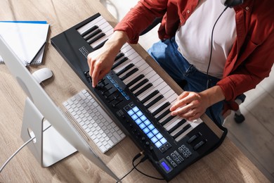 Photo of Man working with MIDI keyboard at wooden table indoors, above view