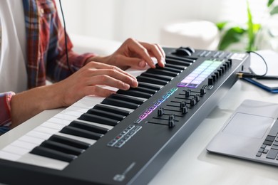 Photo of Man working with MIDI keyboard at white table indoors, closeup