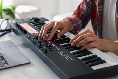 Photo of Man working with MIDI keyboard at white table indoors, closeup