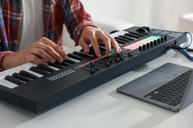 Photo of Man working with MIDI keyboard at white table indoors, closeup