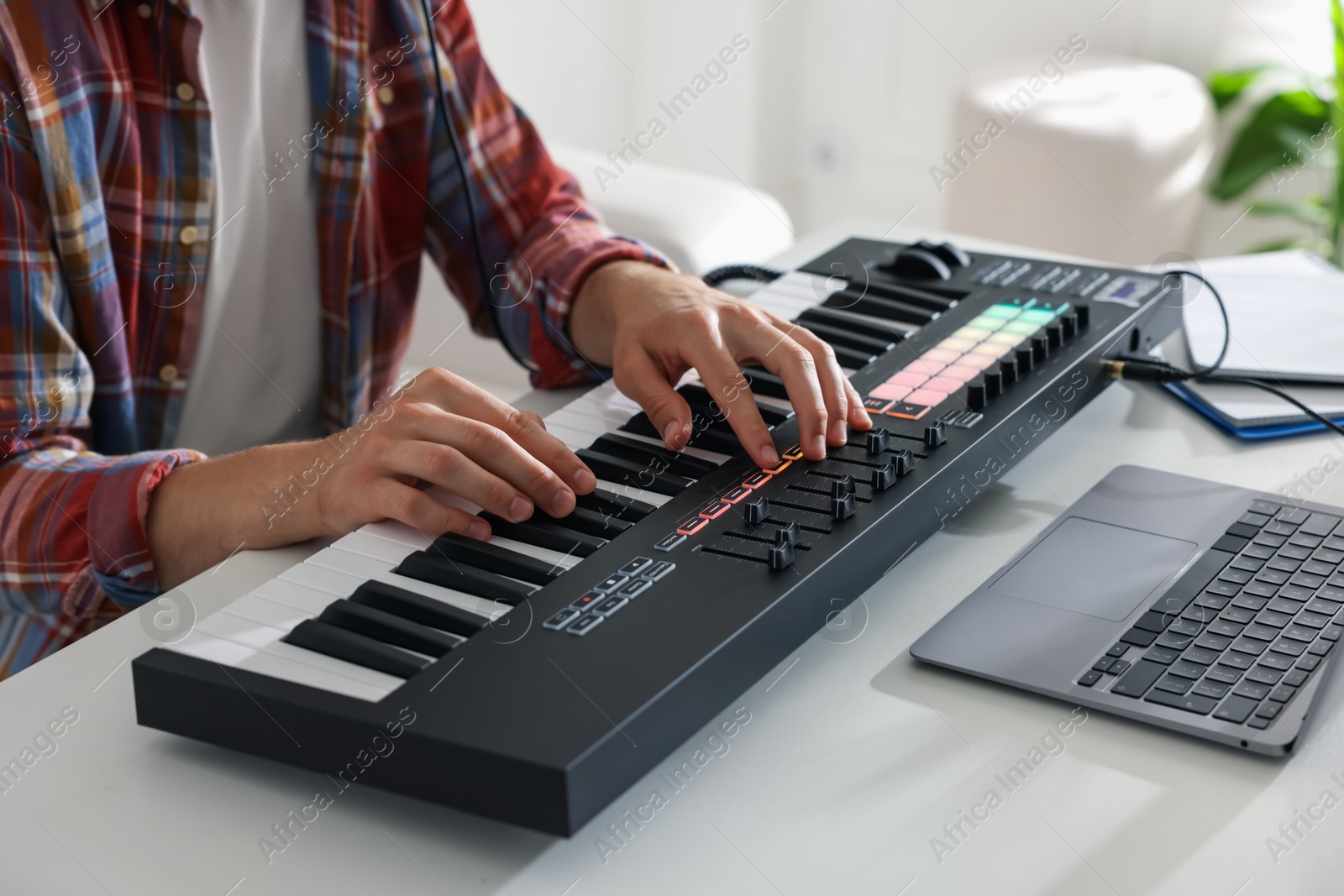 Photo of Man working with MIDI keyboard at white table indoors, closeup