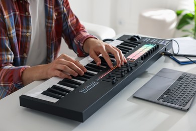 Photo of Man working with MIDI keyboard at white table indoors, closeup