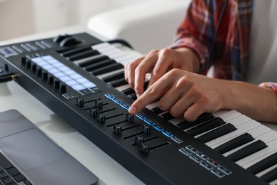 Photo of Man working with MIDI keyboard at white table indoors, closeup