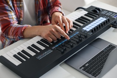 Photo of Man working with MIDI keyboard at white table indoors, closeup