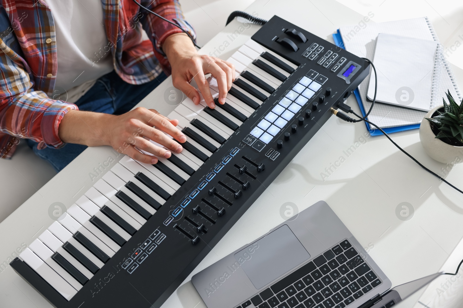 Photo of Man working with MIDI keyboard at white table indoors,